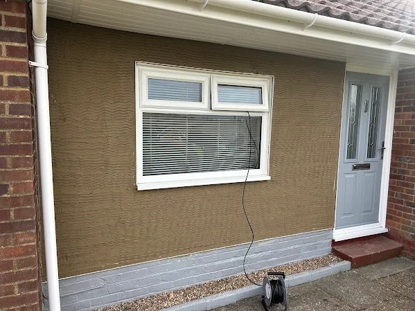 Textured render across the front wall of a house, around a window and a door.