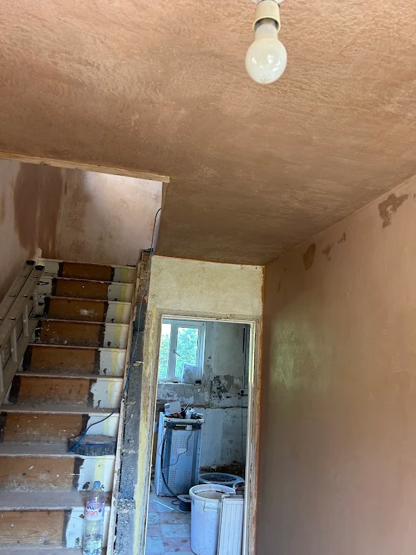 A newly skimmed ceiling above the stairs, with darker patches still drying.